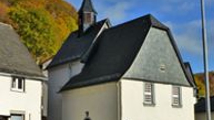 Kleine weiße Kirche mit schwarzem Dach, umgeben von Herbstbäumen.