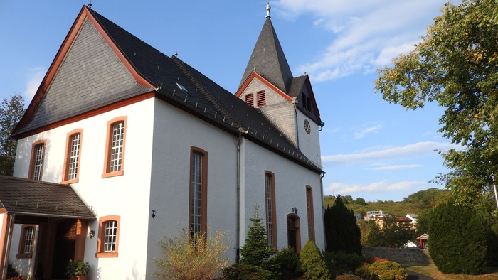Weiße Kirche mit roter Umrandung und Kirchturm, umgeben von Grünflächen.