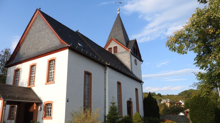 Weiße Kirche mit roter Umrandung und Kirchturm, umgeben von Grünflächen.
