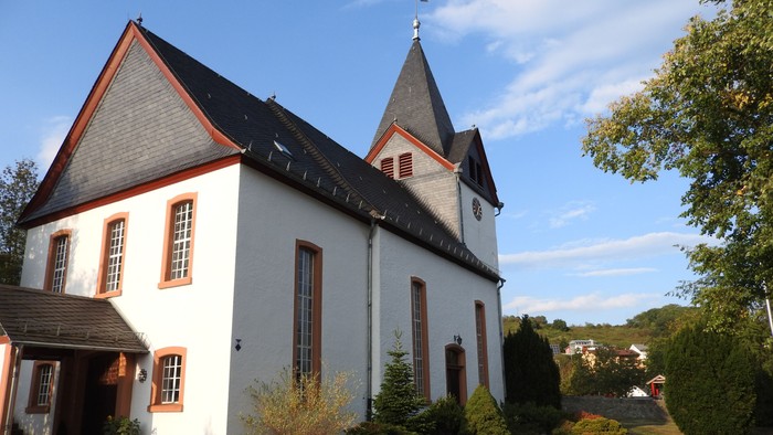 Weiße Kirche mit roter Umrandung und Kirchturm, umgeben von Grünflächen.