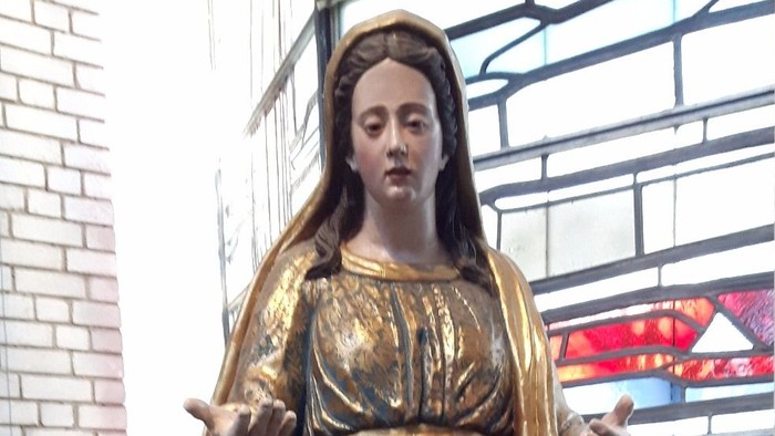 Die Statue einer Frau in einem Kirchenraum mit buntem Glasfenster.