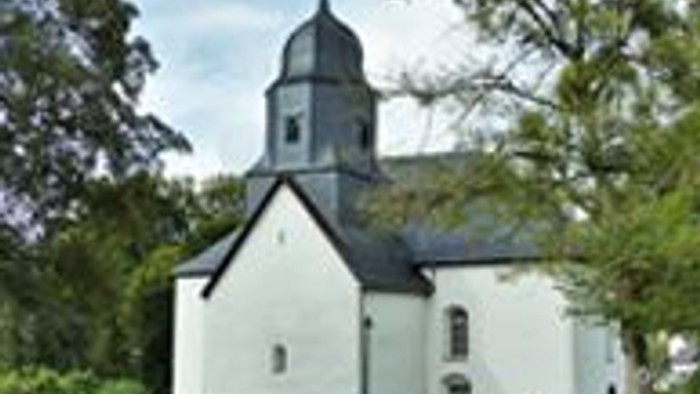 Kleine weiße Kirche mit einem Turm, umgeben von Bäumen.