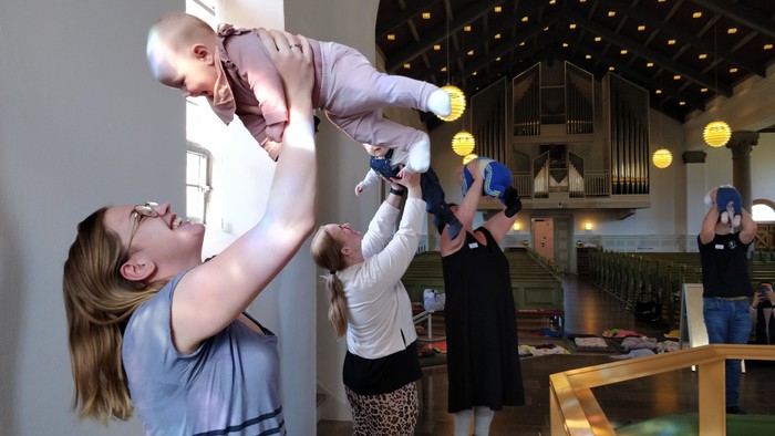 En kvinde holder et barn oppe i en restaurant, mens andre gæster sidder og spiser.