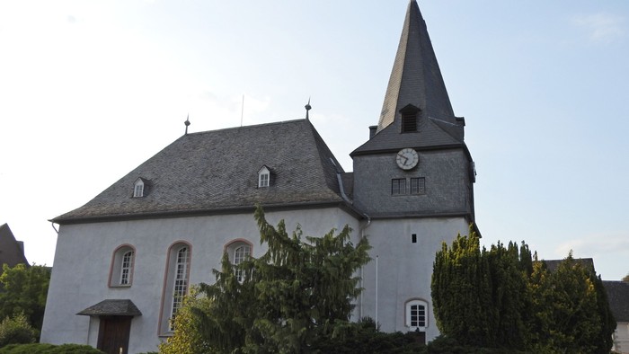 Kirchengebäude mit Uhrturm und grünem Gestrüpp