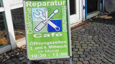 Ein grünes Schild wirbt für ein Reparatur-Café, das am 2. und 4. Mittwoch jedes Monats von 10:30 bis 13:00 Uhr geöffnet ist.