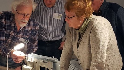 Eine Gruppe untersucht eine alte Nähmaschine mit konzentrierter Aufmerksamkeit und einer hellen Lampe für bessere Sicht.