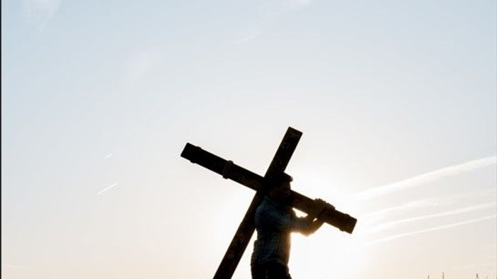 Person trägt Kreuz durch Feld bei Sonnenuntergang