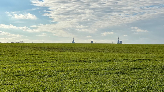 Weites grünes Feld unter blauem Himmel mit einigen Windkraftanlagen in der Ferne