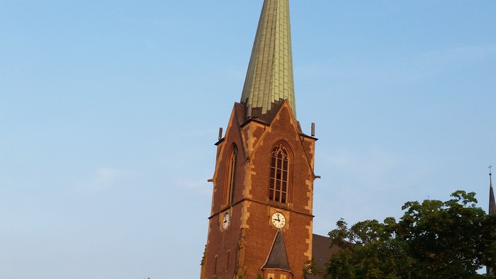 Hohe Kirchturmspitze vor blauem Himmel und Bäumen