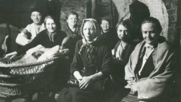 Ein altes Schwarz-Weiß-Familienporträt in einem rustikalen Innenraum mit gewölbten Steinwänden.