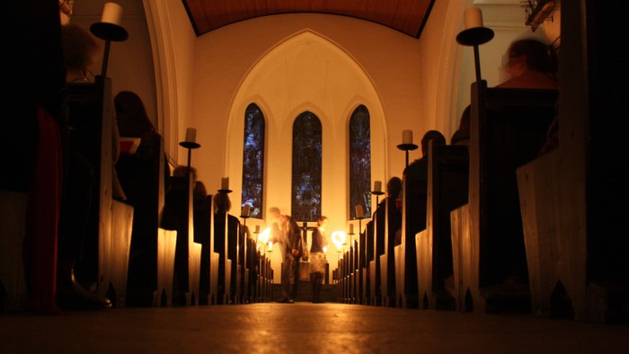 Kirchengang mit brennenden Kerzen, Kirchenfenster im Hintergrund