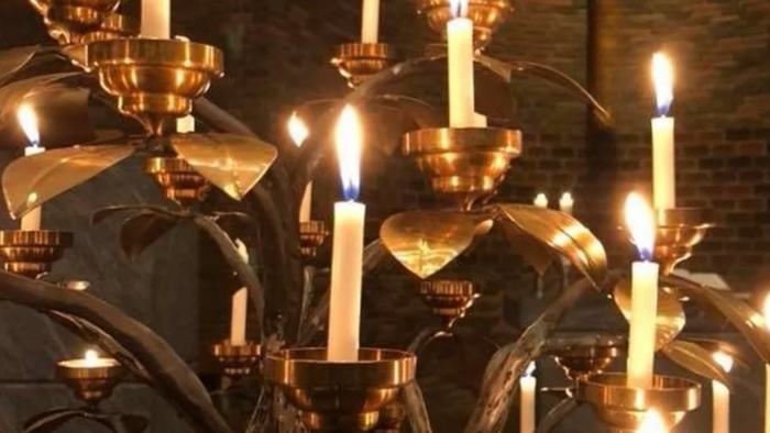 Flere tændte stearinlys i udsmykkede lysestager, sandsynligvis i en kirke eller religiøs sammenhæng.