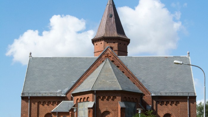 En rød murstenskirke med spir med tårn og vindrosvær.