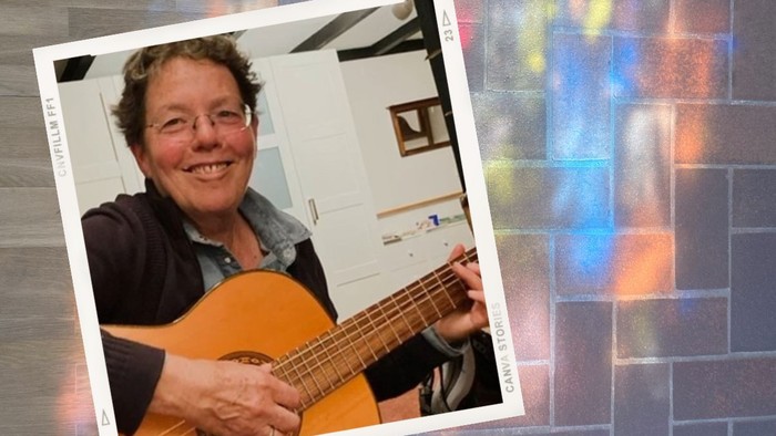 Eine fröhliche Person spielt drinnen eine akustische Gitarre, während im Hintergrund ein farbenfroher, prismenartiger Lichteffekt zu sehen ist.