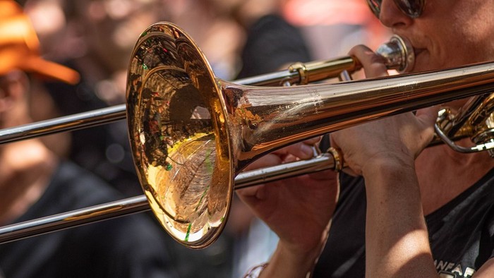 Ein Musiker spielt eine Posaune in einer lebhaften Menschenmenge im Freien.