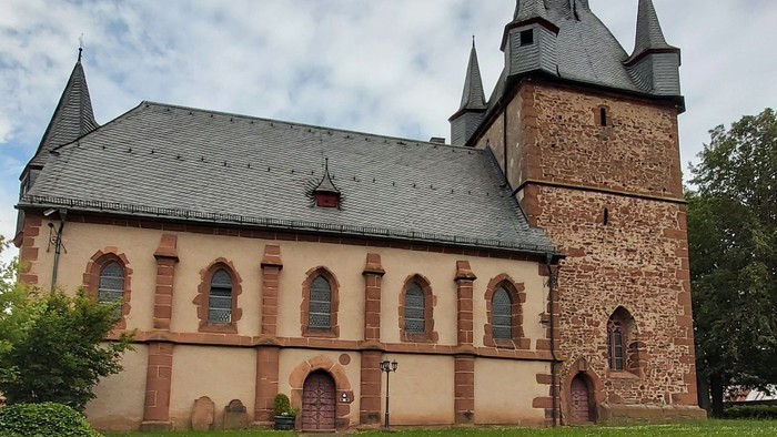 Kirche mit hohem Turmspitz und Rundbogenfenstern, umgeben von grünem Rasen.
