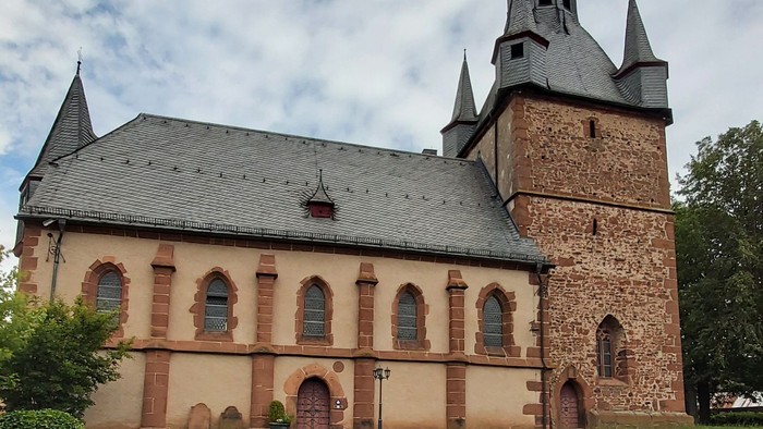 Kirche mit hohem Turmspitz und Rundbogenfenstern, umgeben von grünem Rasen.