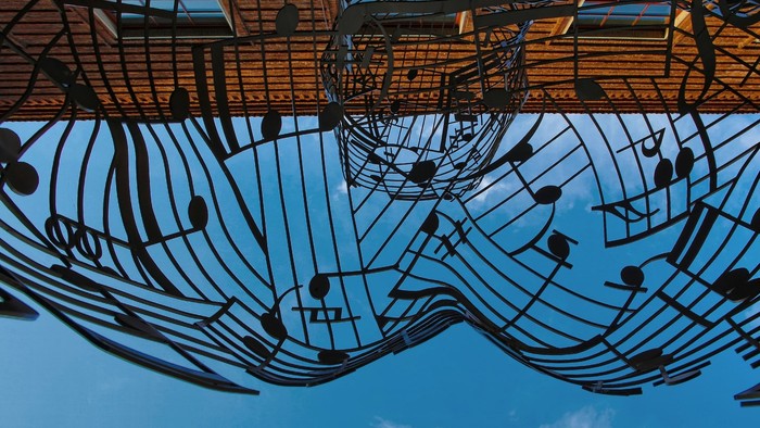 Metallskulptur mit musikalischen Noten, die sich im Wasser spiegeln.