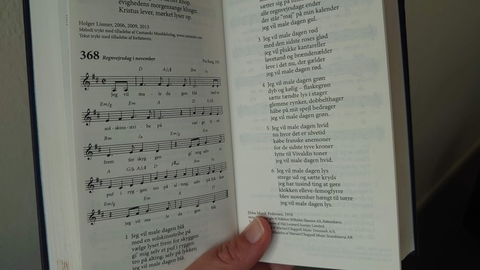 Hånd holder åben bog med noter og tekst på dansk