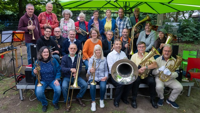 Eine große Gruppe von Musikern posiert mit ihren Instrumenten unter einem grünen Sonnenschirm im Freien