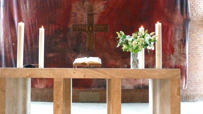 Ein hölzerner Altar mit Kreuz, Kerzen und Blumen vor rotem Hintergrund
