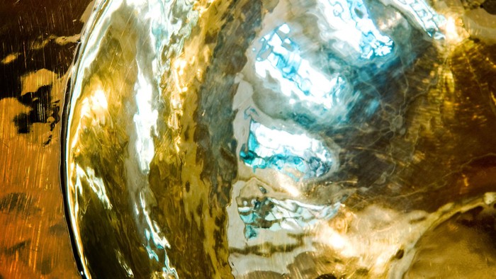 Eine Nahaufnahme einer glänzenden, gealterten Messingschale, die bunte abstrakte Muster reflektiert.