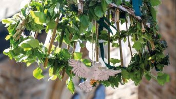 Ein Vogel sitzt zwischen üppigen grünen Blättern auf einem Baumast, umgeben von hängenden Dekorationsgegenständen.