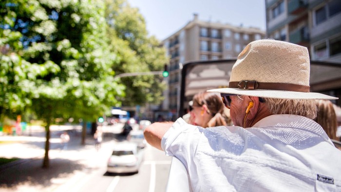 Ein Mann mit Hut und Sonnenbrille sitzt auf einer Bank und schaut auf eine belebte Straße.