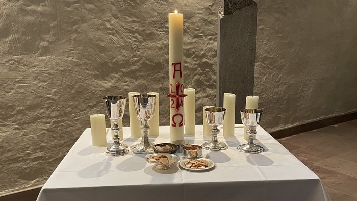 Elegante Altar-Anordnung mit Kerzen, Weingläsern, Brot und einer hohen brennenden Kerze mit griechischen Buchstaben.