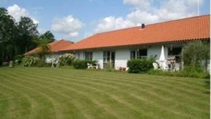 En hvid villa med rød tag og grønne omgivelser