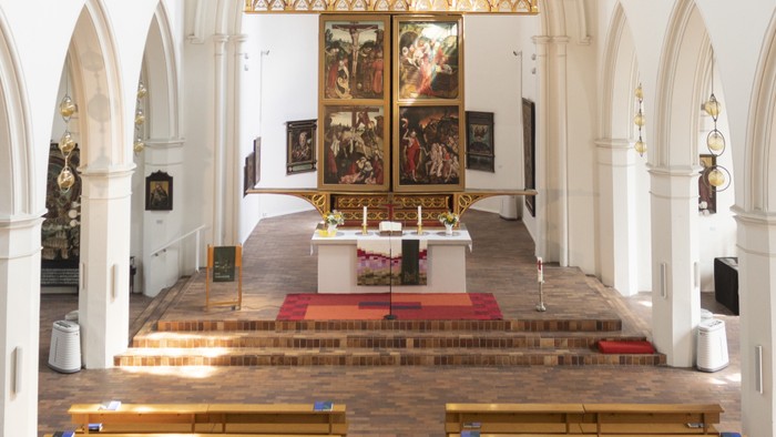 Mittelschiff einer Kirche mit Blick auf den Altar, hölzerne Kirchenbänke im Vordergrund.