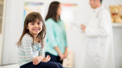 Ein kleines Mädchen sitzt in einem Arztzimmer und lächelt.