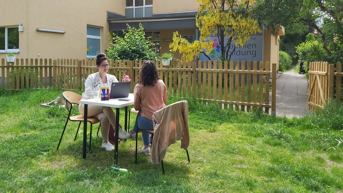 Zwei Personen sitzen im Garten vor einem Haus und arbeiten an einem Laptop.