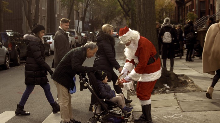 En gruppe mennesker, heriblandt en mand i Santa-kostume, træffer en gade med en babyvogn.