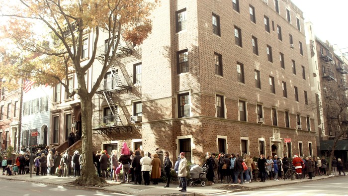 En lang kø af mennesker står foran et stort, rødt murstenshus.