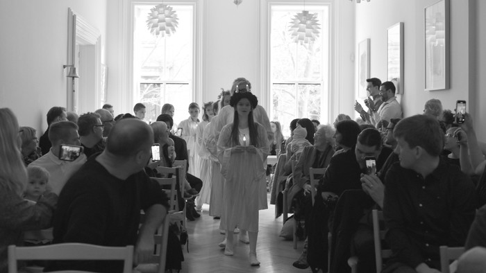 En gruppe af mennesker samles i et lys rum med store vinduer og hængende dekorationer.