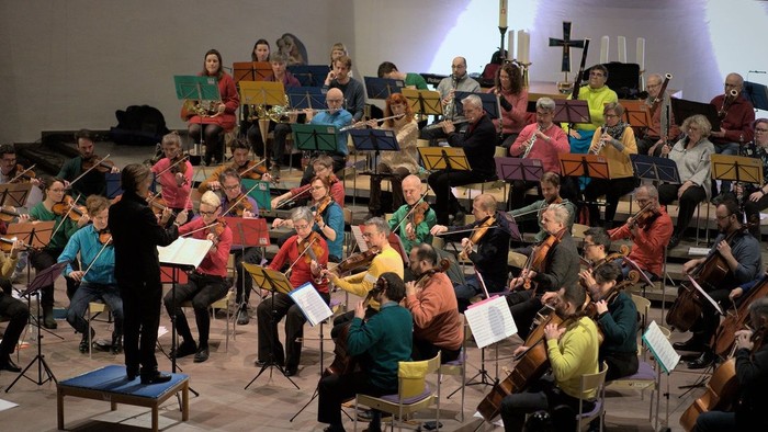 Ein großer Chor proben in einer Kirche unter der Leitung eines Dirigenten.