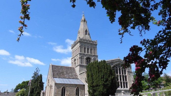 Church with tall spire and graveyard, framed by tree branches