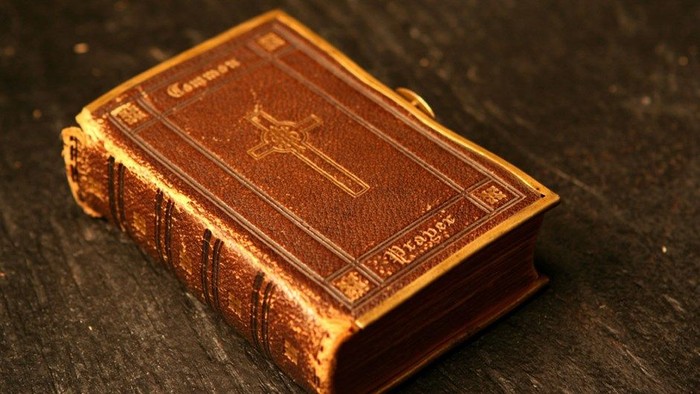 An old book with a worn cover and cross design lies on a dark surface.
