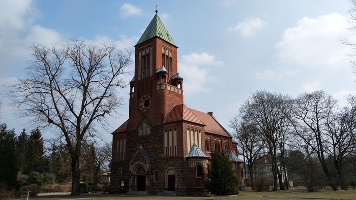 Ein rotes Backsteingebäude mit Uhrturm und spitzem Dach in einem Park.
