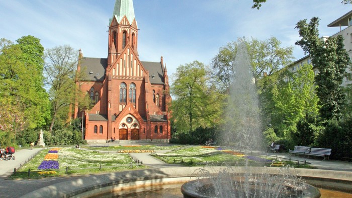 Ein rotes Kirche mit hohem Turm und ein Brunnen im Vordergrund