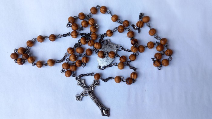 Ein Rosenkranz mit Holzperlen und silbernem Kreuz liegt auf einem weißen Tuch.