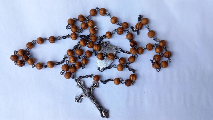 Ein Rosenkranz mit Holzperlen und silbernem Kreuz liegt auf einem weißen Tuch.