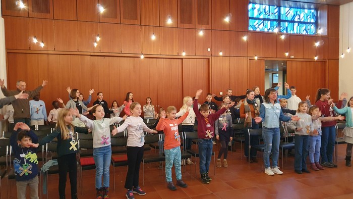 Kinder, die in einer Gruppe singen, während Erwachsene zuschauen.