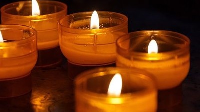 Mehrere brennende Kerzen in Glashaltern, die eng beieinander aufgestellt sind.