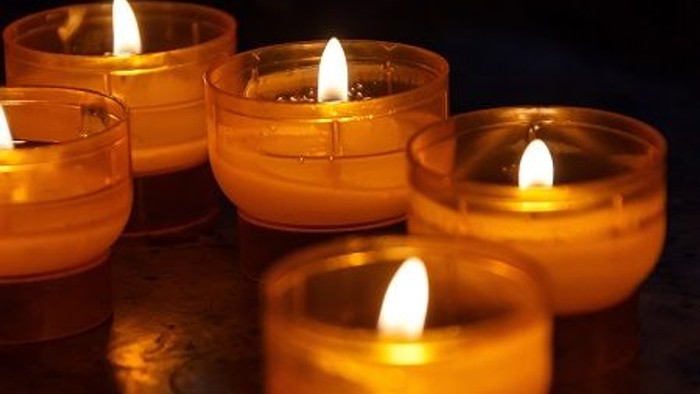 Mehrere brennende Kerzen in Glashaltern, die eng beieinander aufgestellt sind.