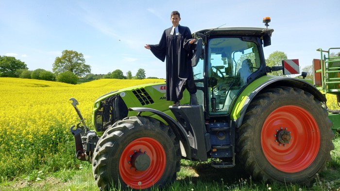 Der Pastor steht auf einem großen Trecker.