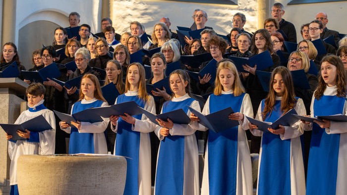 Ein vielfältiger Chor singt harmonisch in einer Kirche, wobei die Sänger in abgestimmten blauen und weißen Roben gekleidet sind.