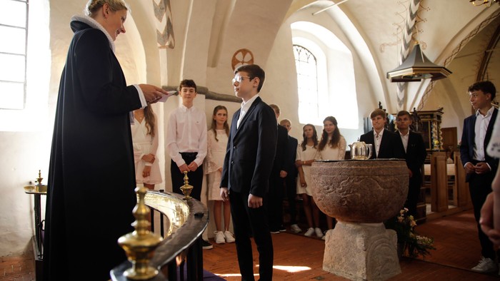 En præst udfører en ceremoni i en kirke, mens en gruppe mennesker ser til.