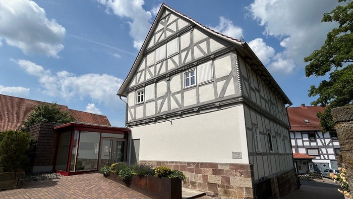 Traditionelles Fachwerkhaus mit modernem Glasanbau, umgeben von einem Ziegelhof und Grünflächen.